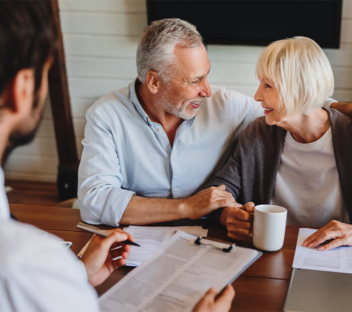 Elderly couple smiling and looking at each other while in a consultation in their home.